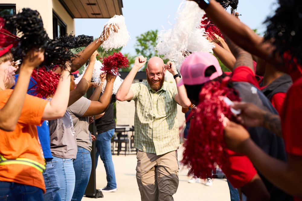 Celebratory moment with crowd waving pom-poms creating festive tunnel at outdoor event.