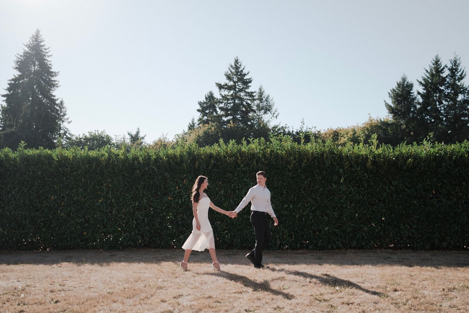 Couple walking together during a wedding engagement shoot outside with the groom leading the bride.