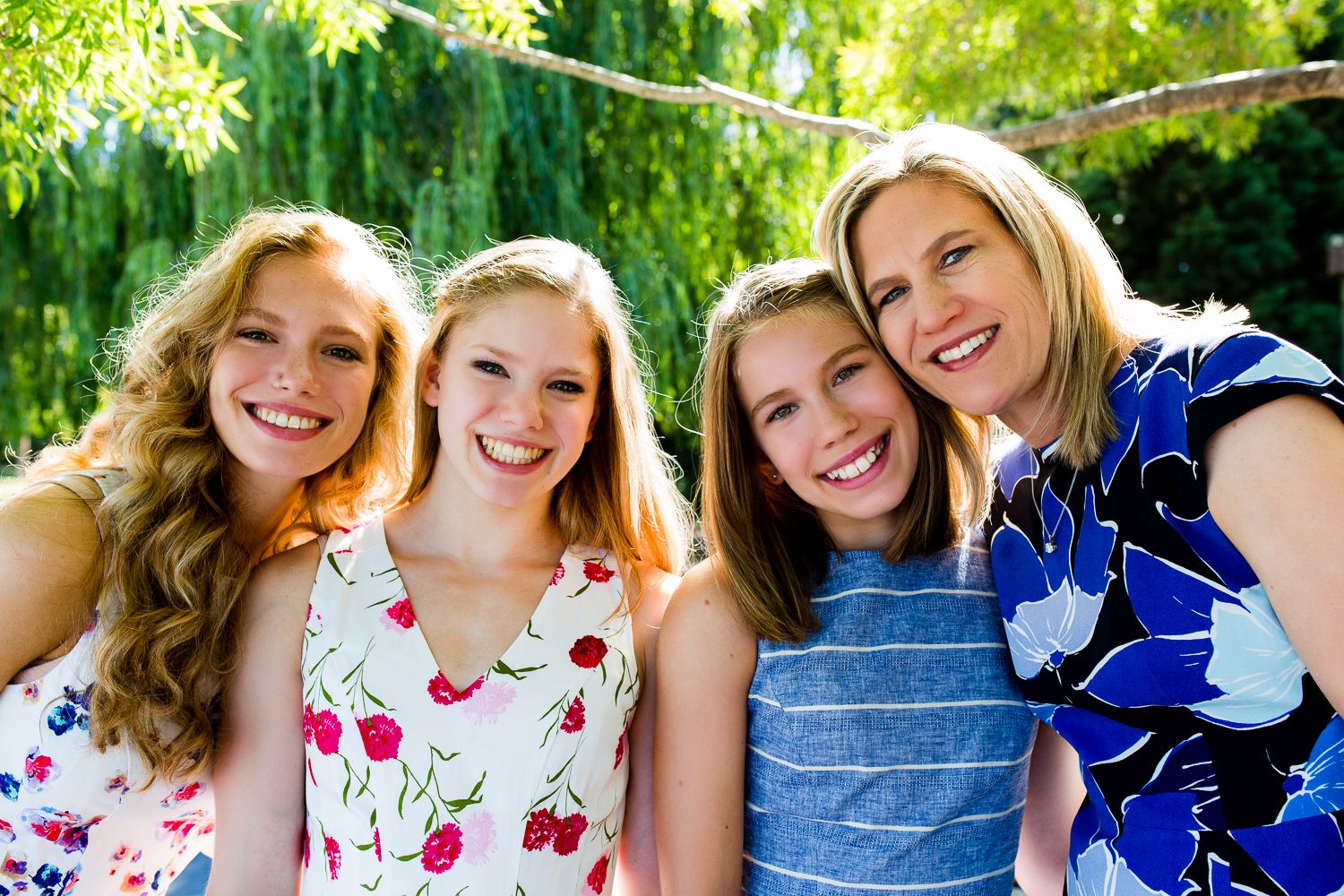 Four people smiling together outdoors in front of lush green willow trees.
