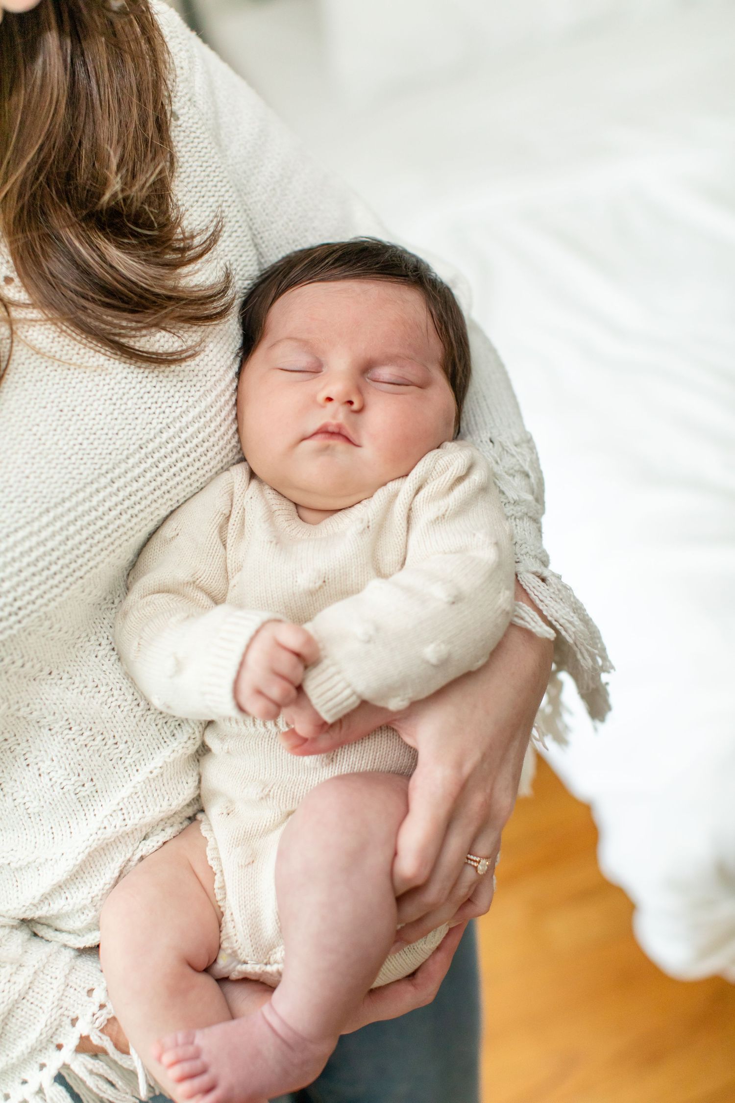 A sleeping baby in cream-colored clothing rests peacefully against a white knit sweater.