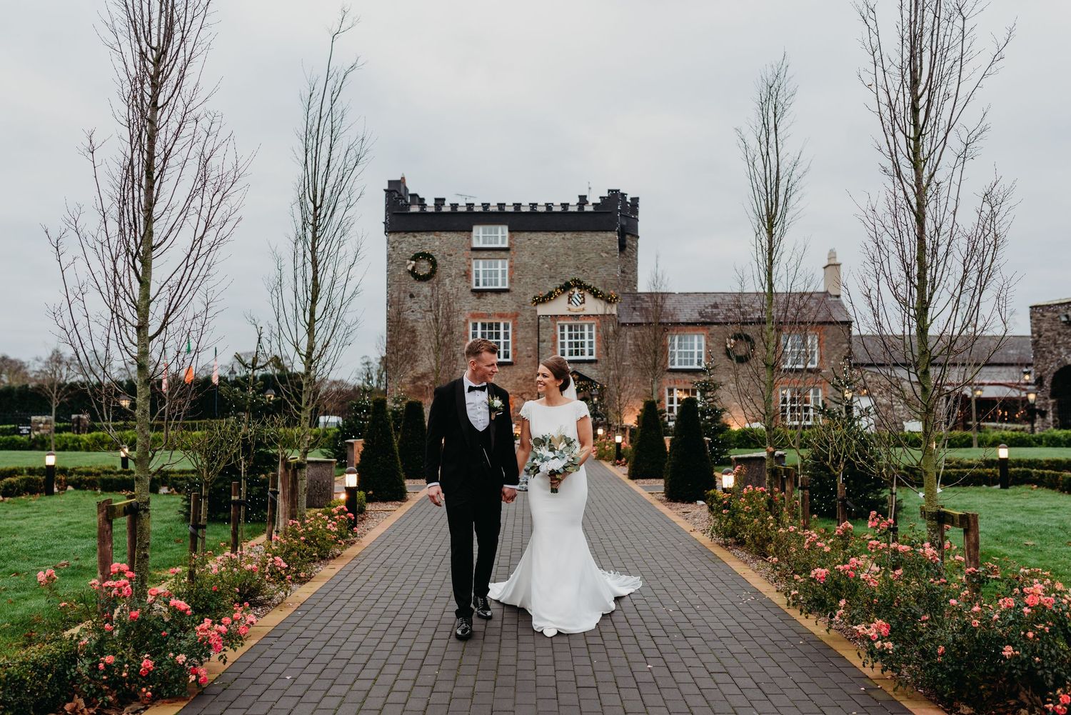 Bride and Groom walking towards the camera, holding hands and very happy, with Darver Castle behind them.