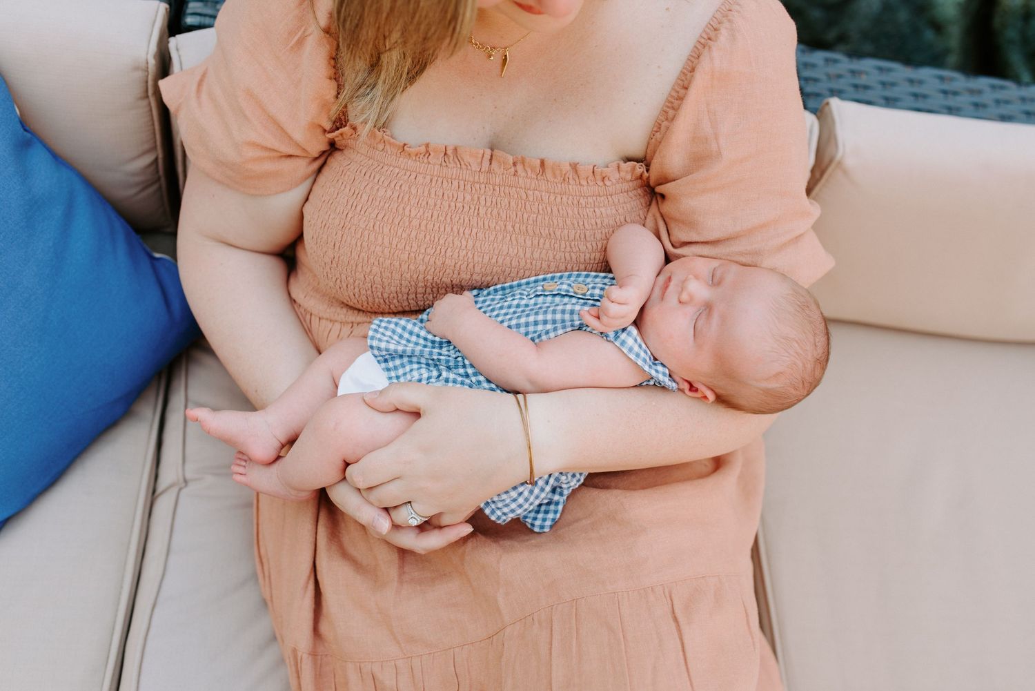 Parent in peach sweater cradling sleeping newborn in blue outfit.