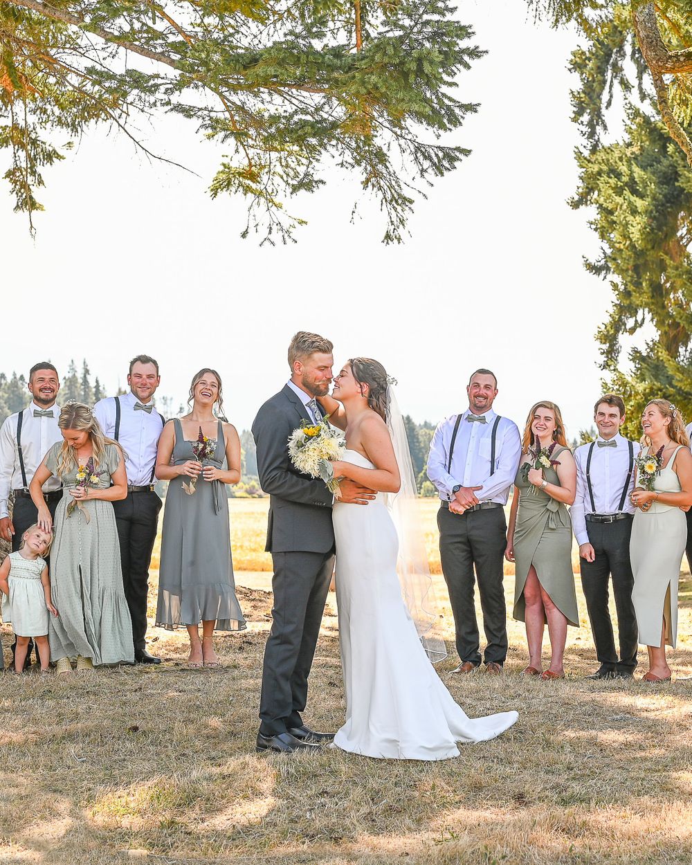 Bride and groom kiss while wedding party look on.