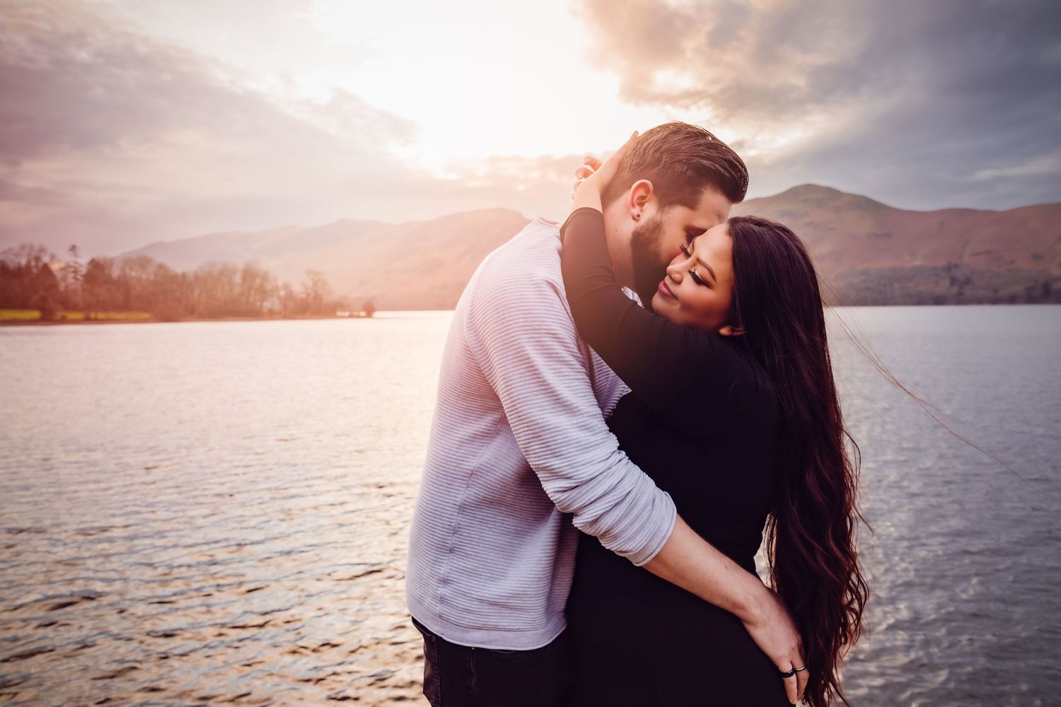 Intimate couple embracing by a lake during golden hour sunset.
