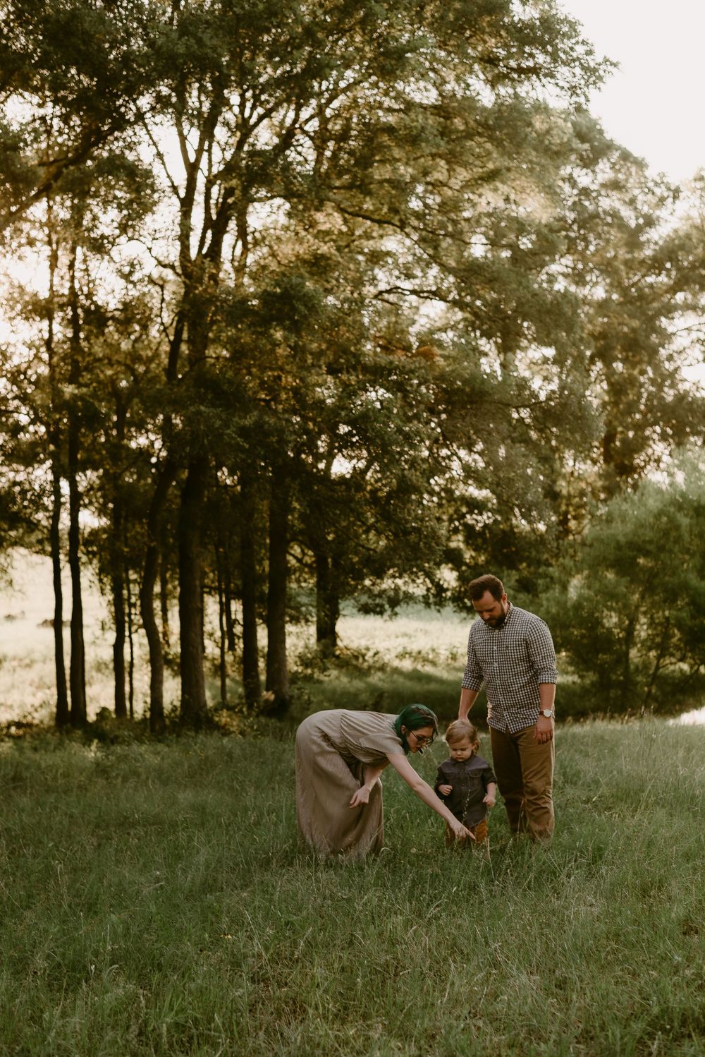 Family enjoying outdoor activities together in a sunlit meadow surrounded by trees.