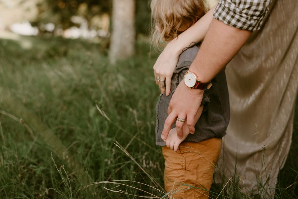 Close-up view of parent holding small child wearing brown boots in grassy meadow.