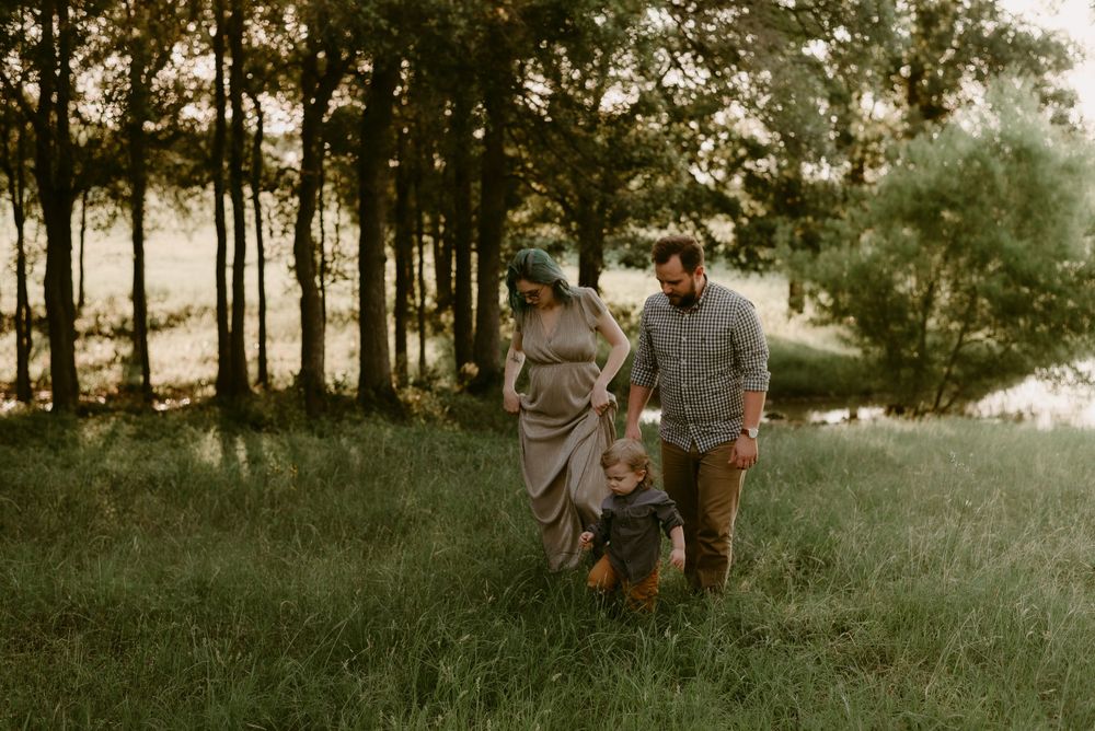 Family walking together through a scenic meadow at sunset with trees in background.