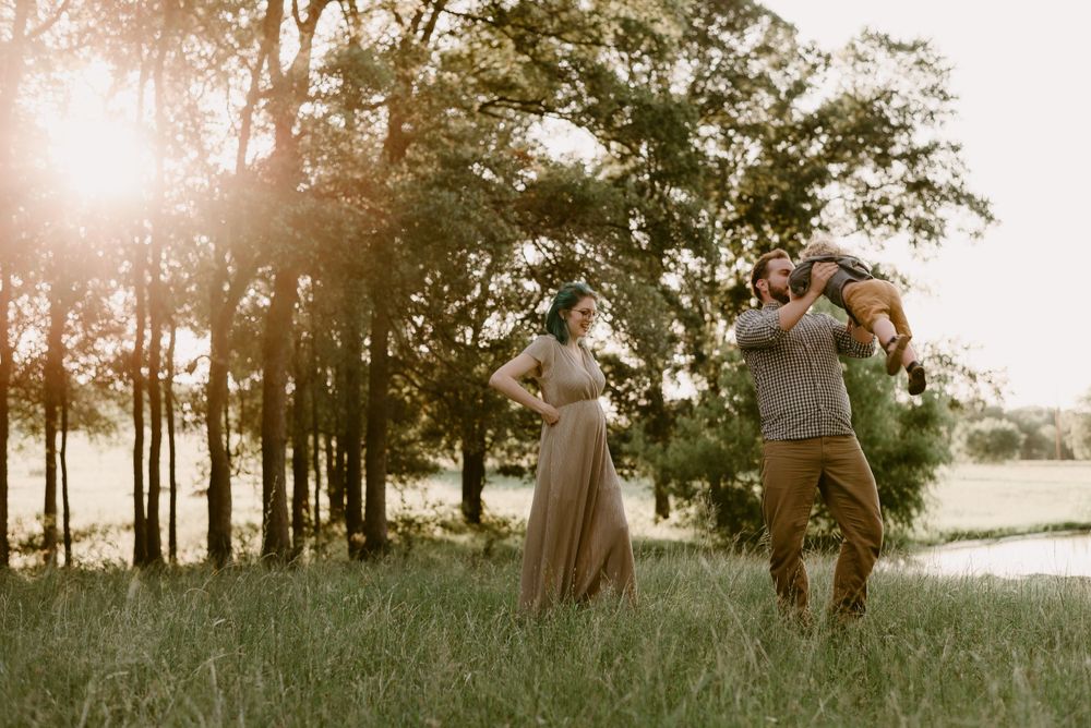 Couple enjoying playful moment together in sunlit meadow with trees in background.