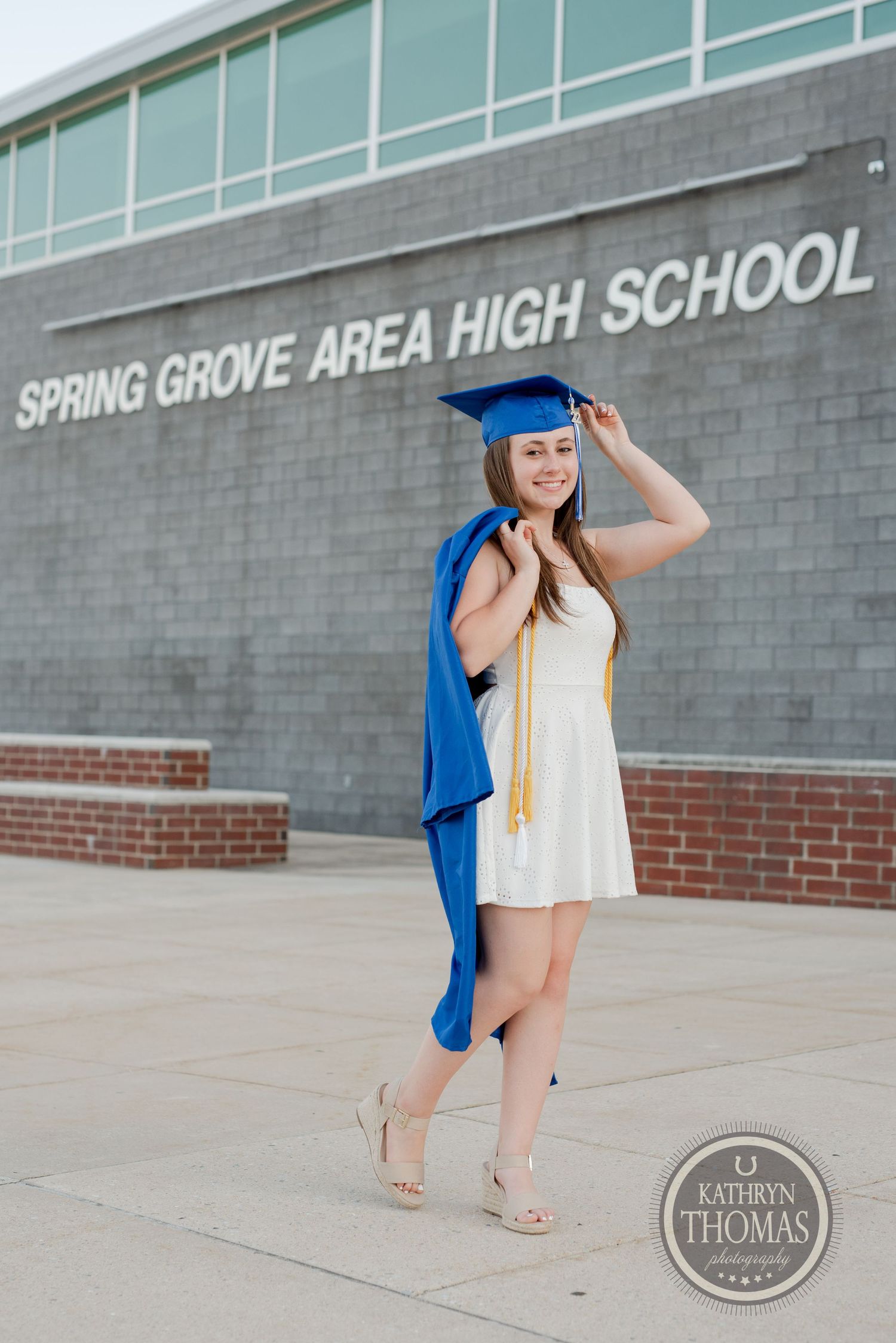 Graduate stands outside Spring Grove Area High School in white dress and blue graduation attire.