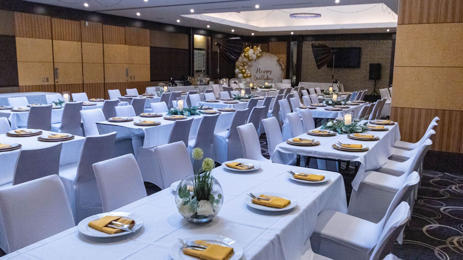 Elegant banquet hall setup with white chairs and place settings at round tables.