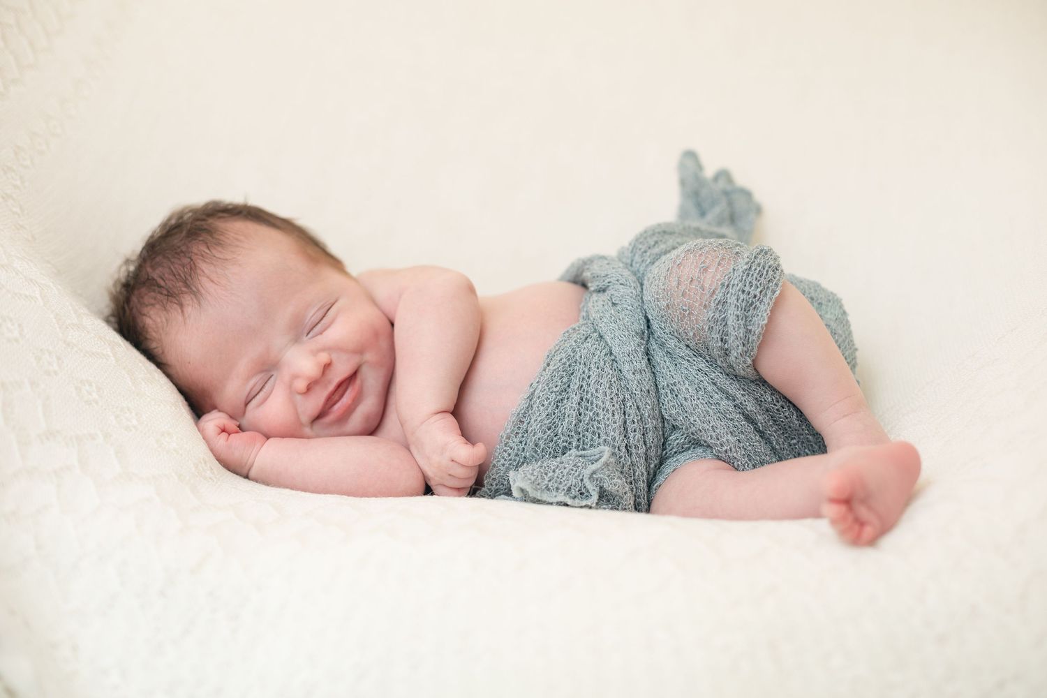 Peaceful newborn photo series showing a sleeping baby wrapped in soft blue knit on white background.