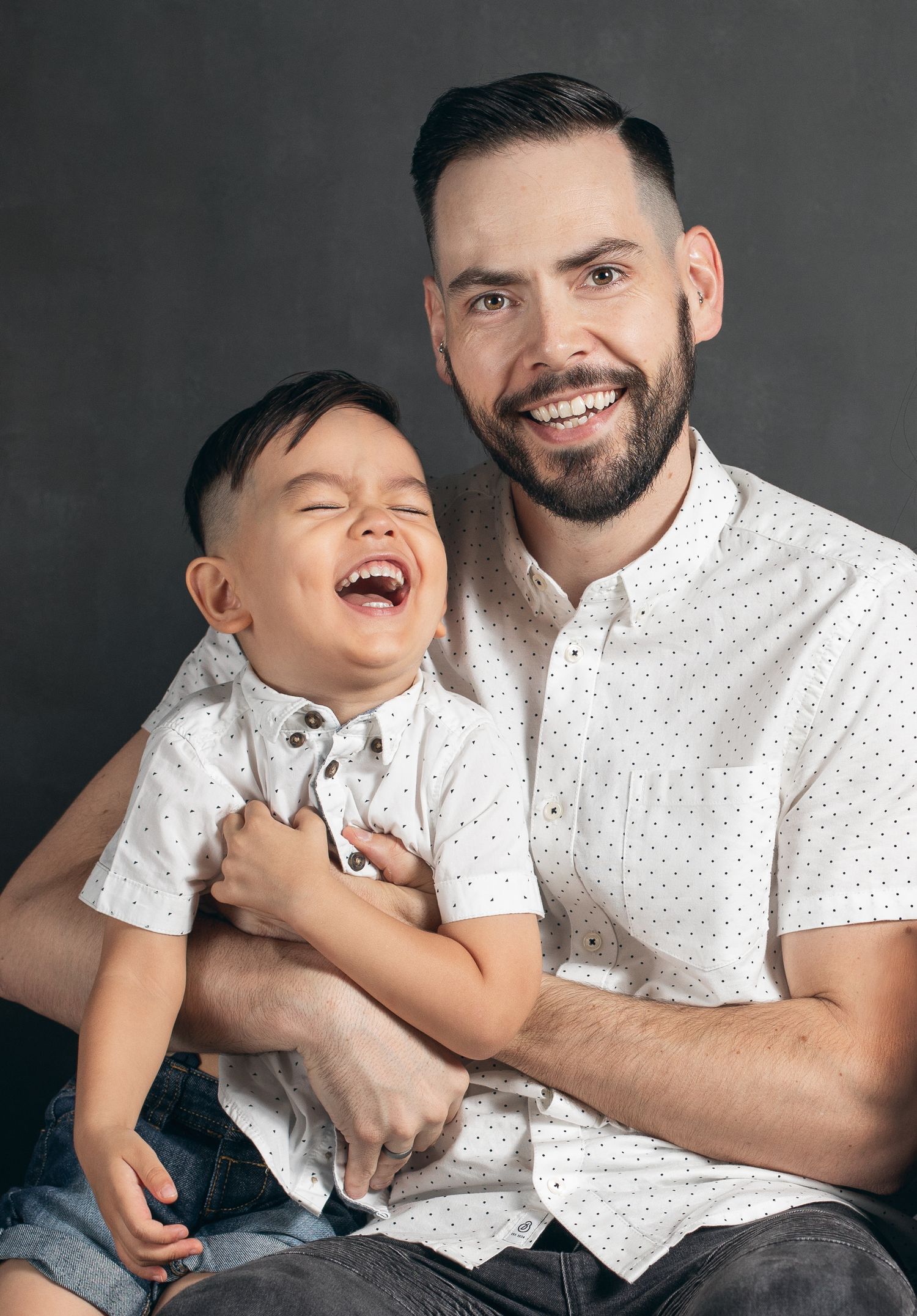 Candid studio portrait showing playful interactions and laughter between father and son in matching white polka dot shirts.