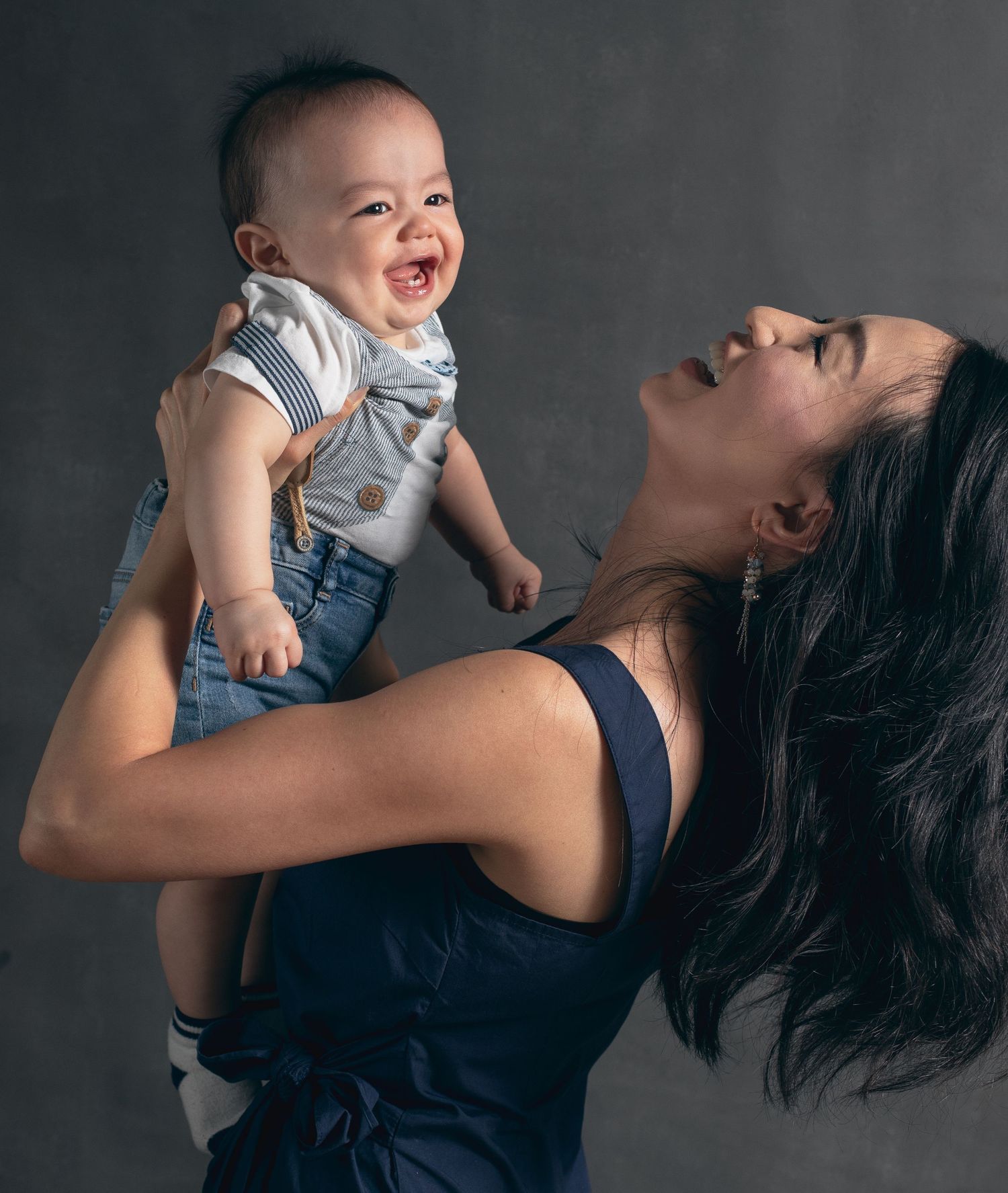 A joyful portrait of a parent playfully lifting and interacting with a baby against a dark studio background.