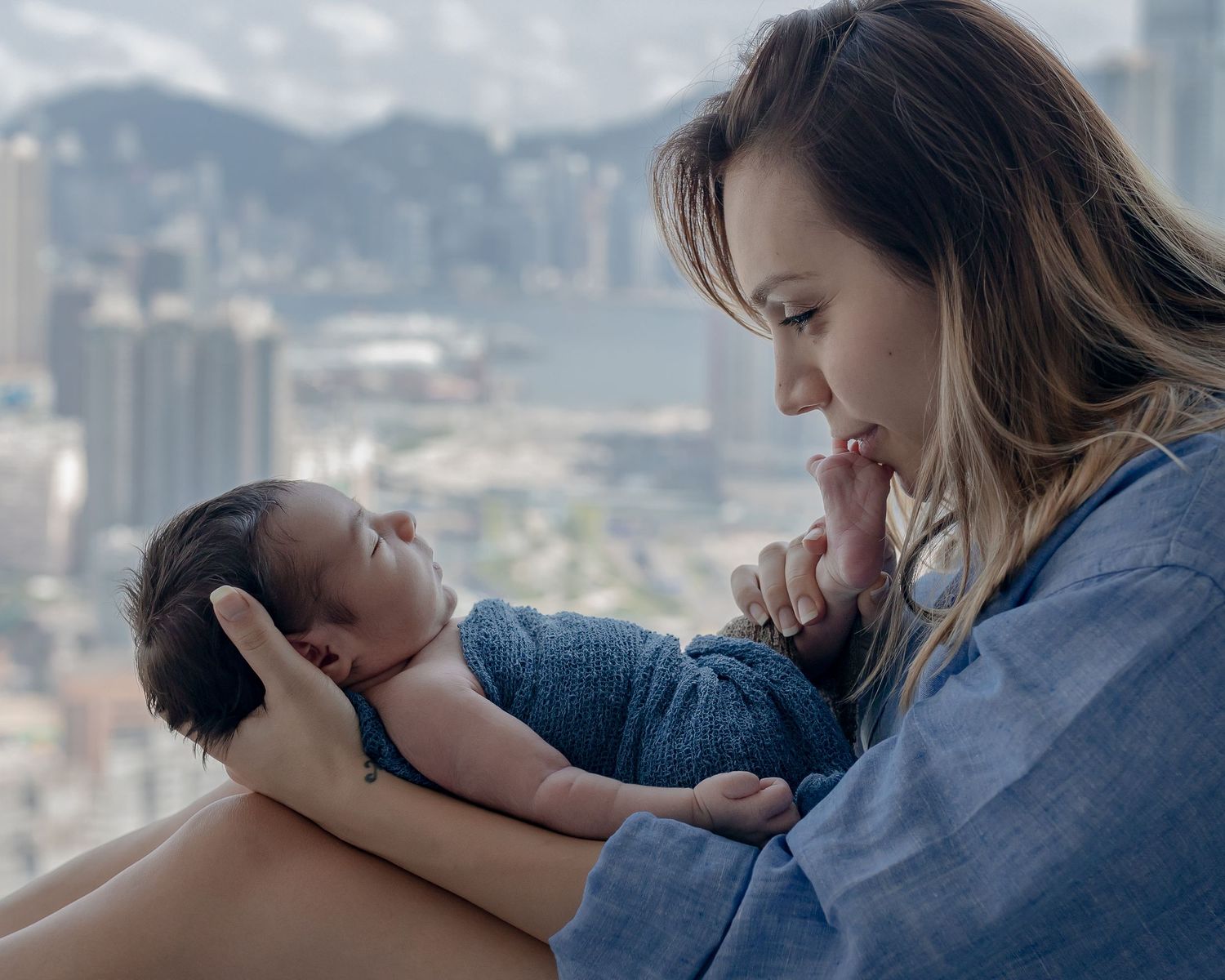 Intimate moment between parent and infant with city skyline visible through window.