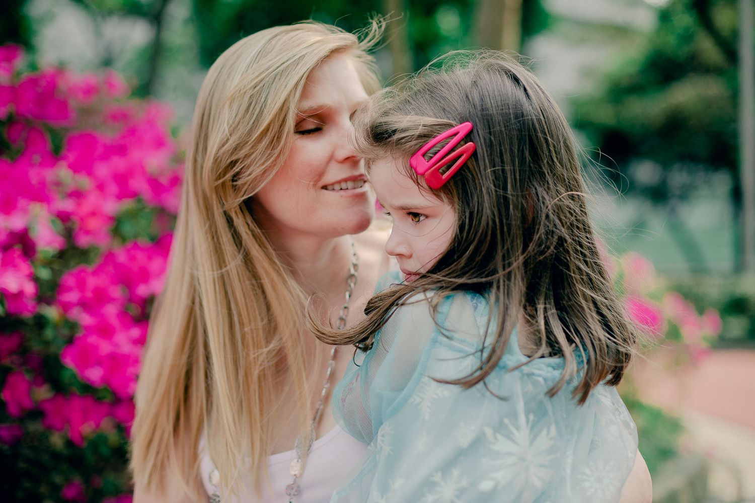 Sweet outdoor portraits showing affectionate moments between mother and daughter surrounded by vibrant pink flowers.