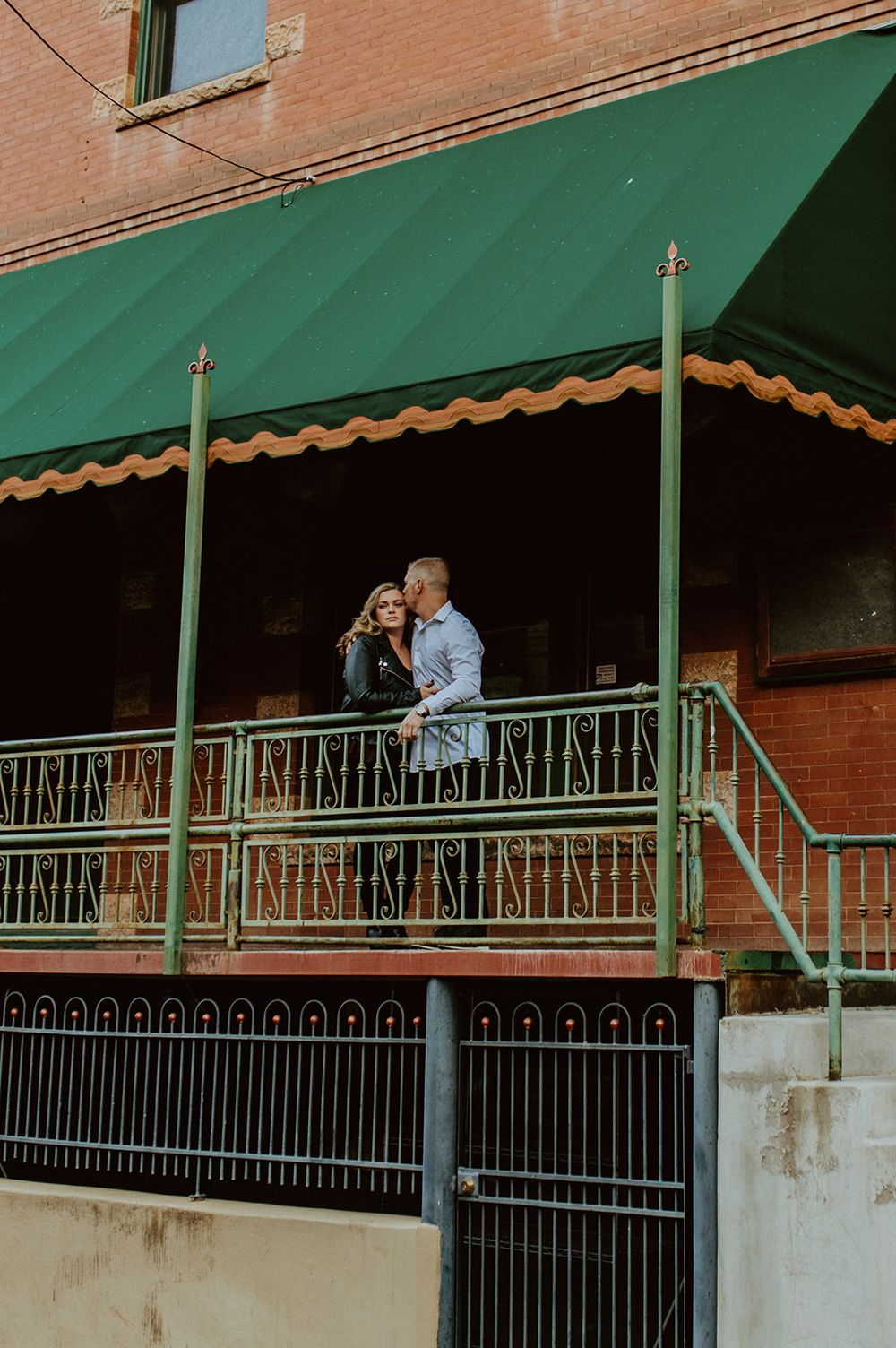 A romantic moment captured on a balcony under a green awning of a historic downtown building.
