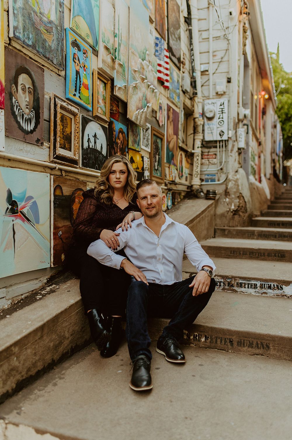A couple poses on urban steps surrounded by colorful street art and murals.