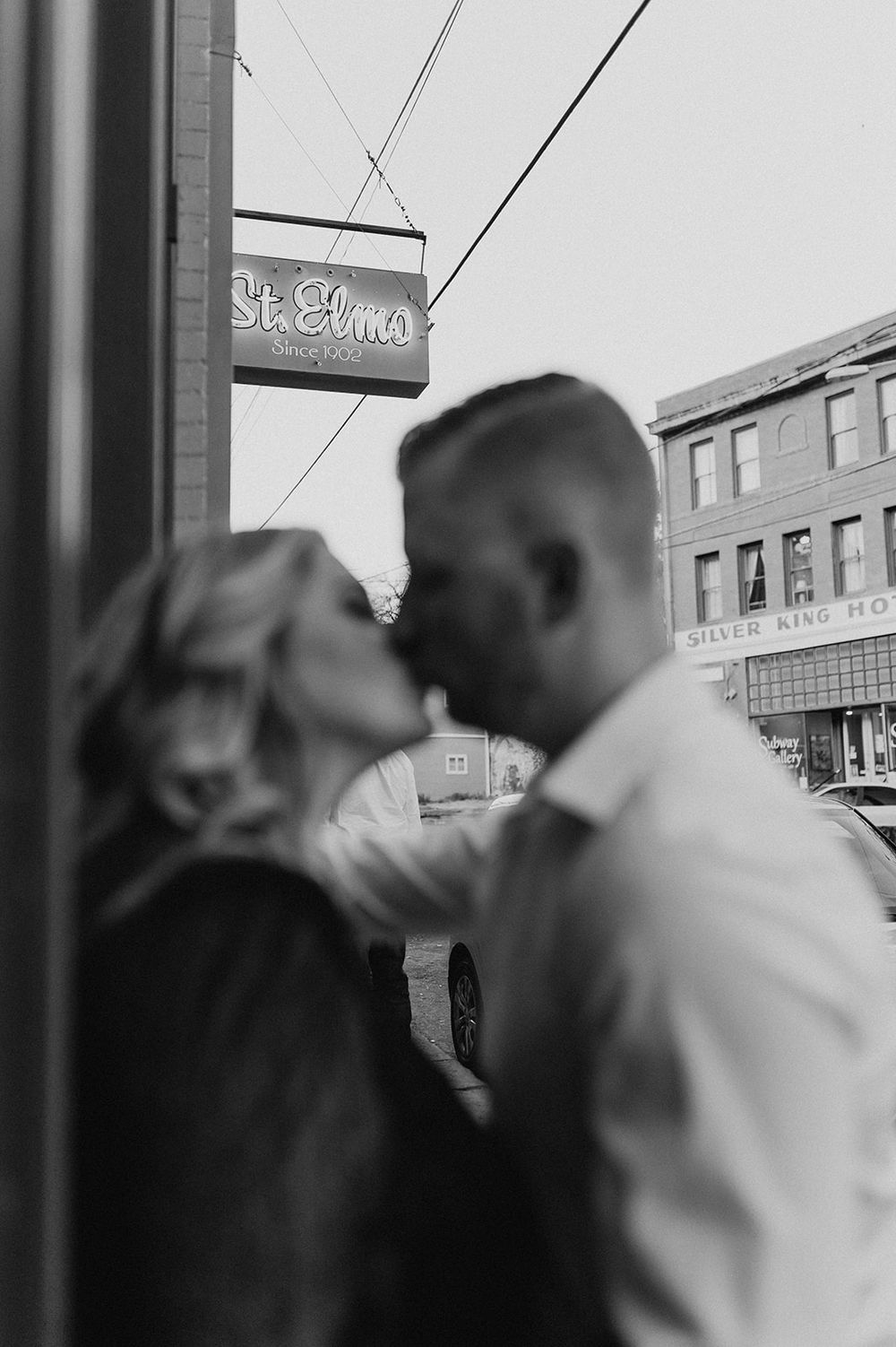 A black and white photograph of a couple embracing near a storefront.