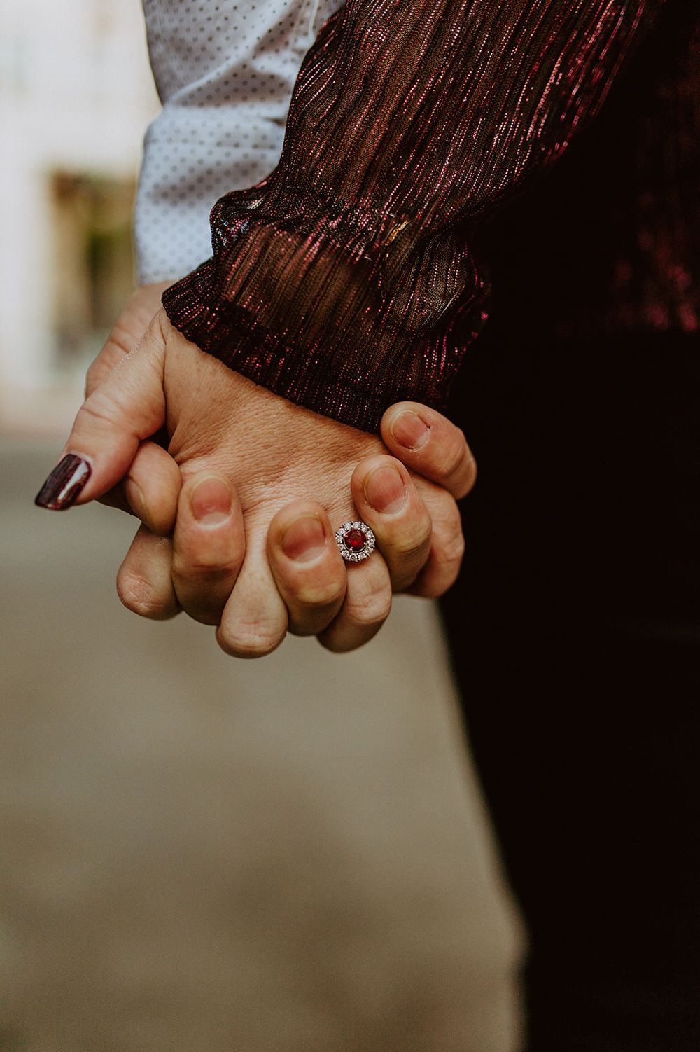 Close-up of clasped hands showing an engagement ring with dark clothing in the background.