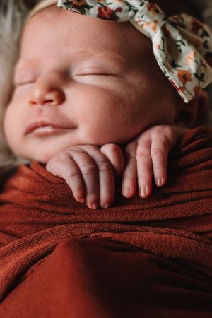 Sleeping baby in floral headband wrapped in rust colored textile.