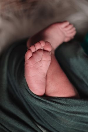 Close-up of tiny newborn baby feet wrapped in dark green fabric.
