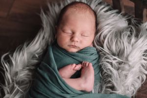 Sleeping newborn wrapped in teal green swaddle on fluffy white fur.