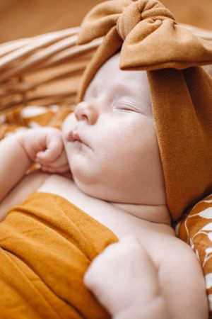 Peaceful sleeping baby in caramel swaddle with matching bow headband.