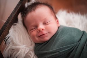Peaceful sleeping newborn baby swaddled in green wrap on soft white fur backdrop.