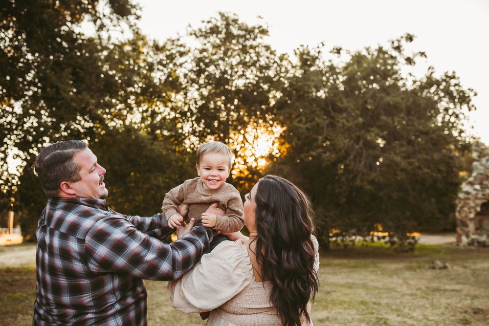 young son is put up in the air like an airplane while mom and dad look on and smile
