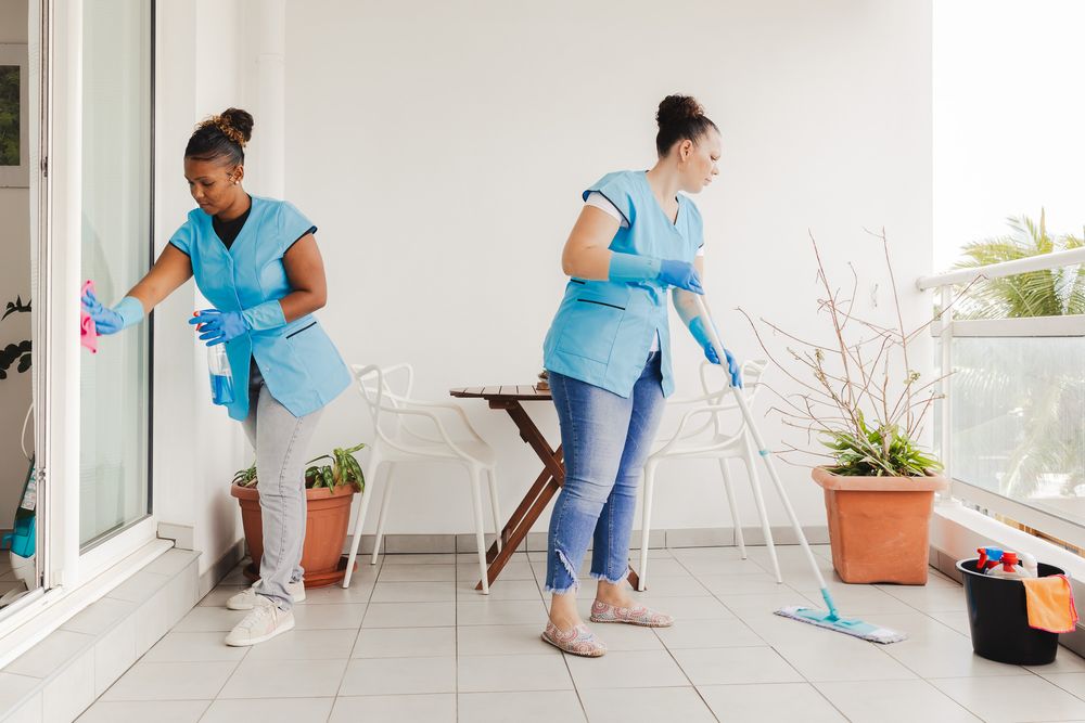Two cleaners in blue uniforms working together to clean outdoor patio area.