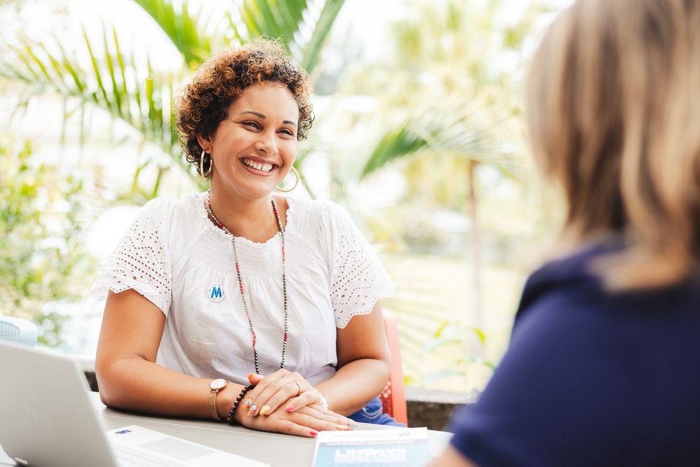 Professional meeting taking place in a bright tropical setting with palm trees visible through windows.