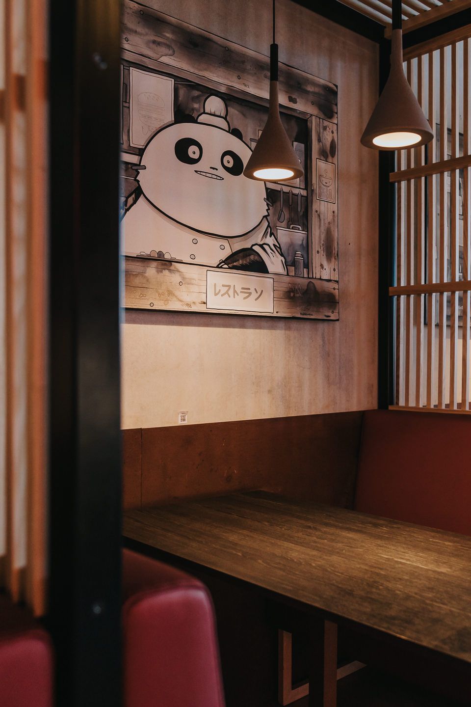 Empty wooden dining tables with red chairs in a restaurant featuring panda artwork on the wall.