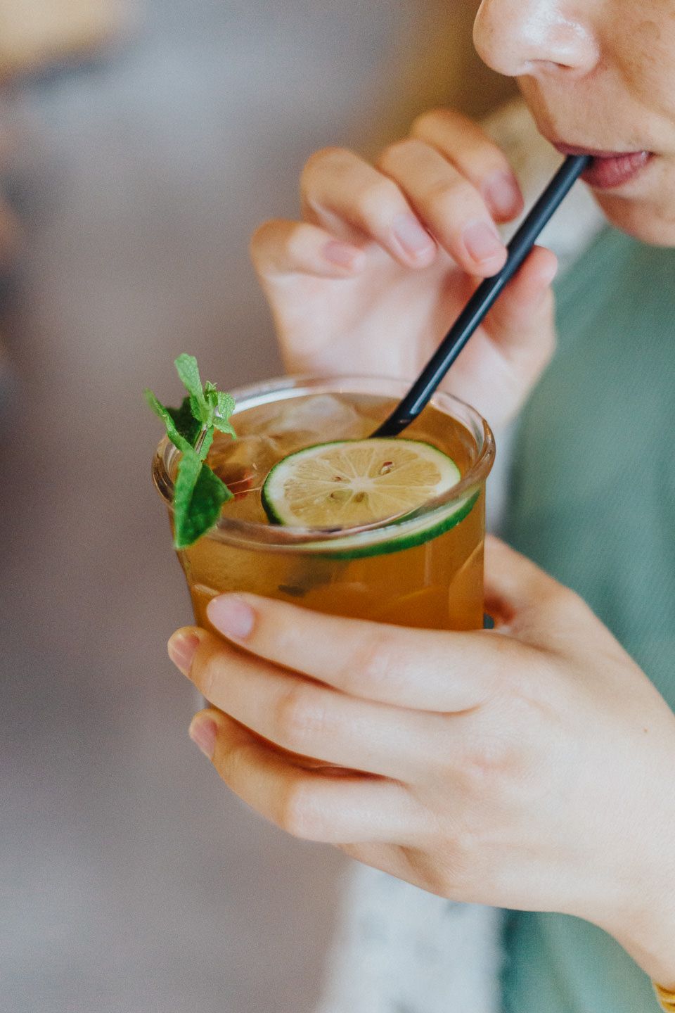 Close-up shots of hands holding a garnished cocktail with mint leaves and a straw.
