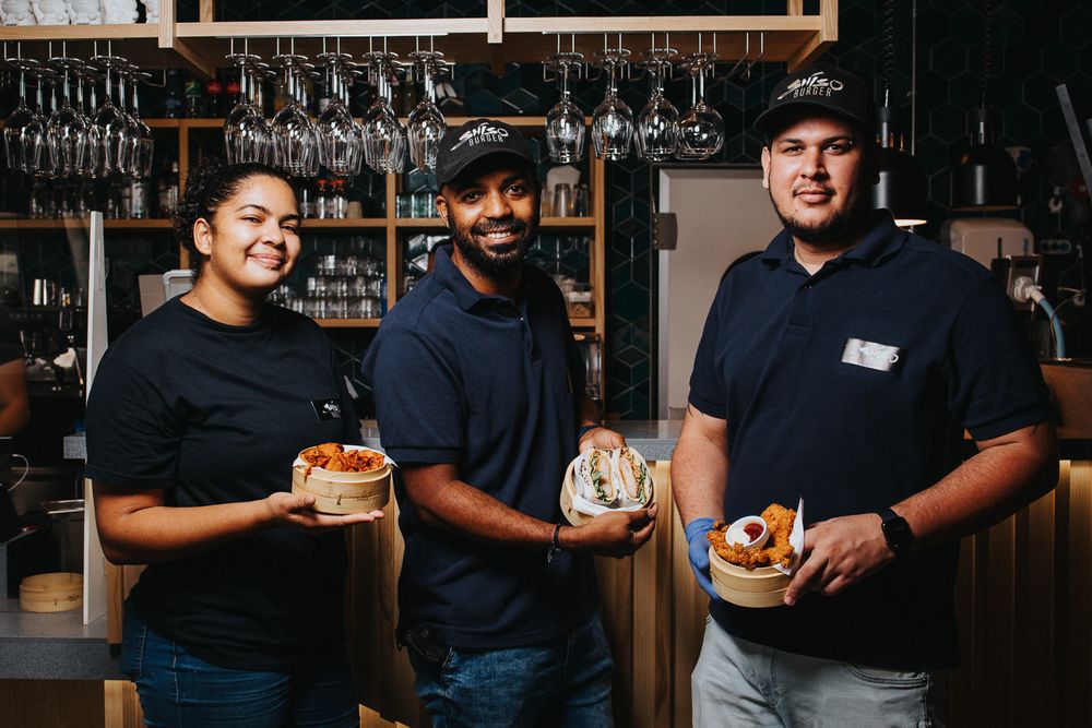 Restaurant staff in black uniforms serving food and drinks at a bar counter.
