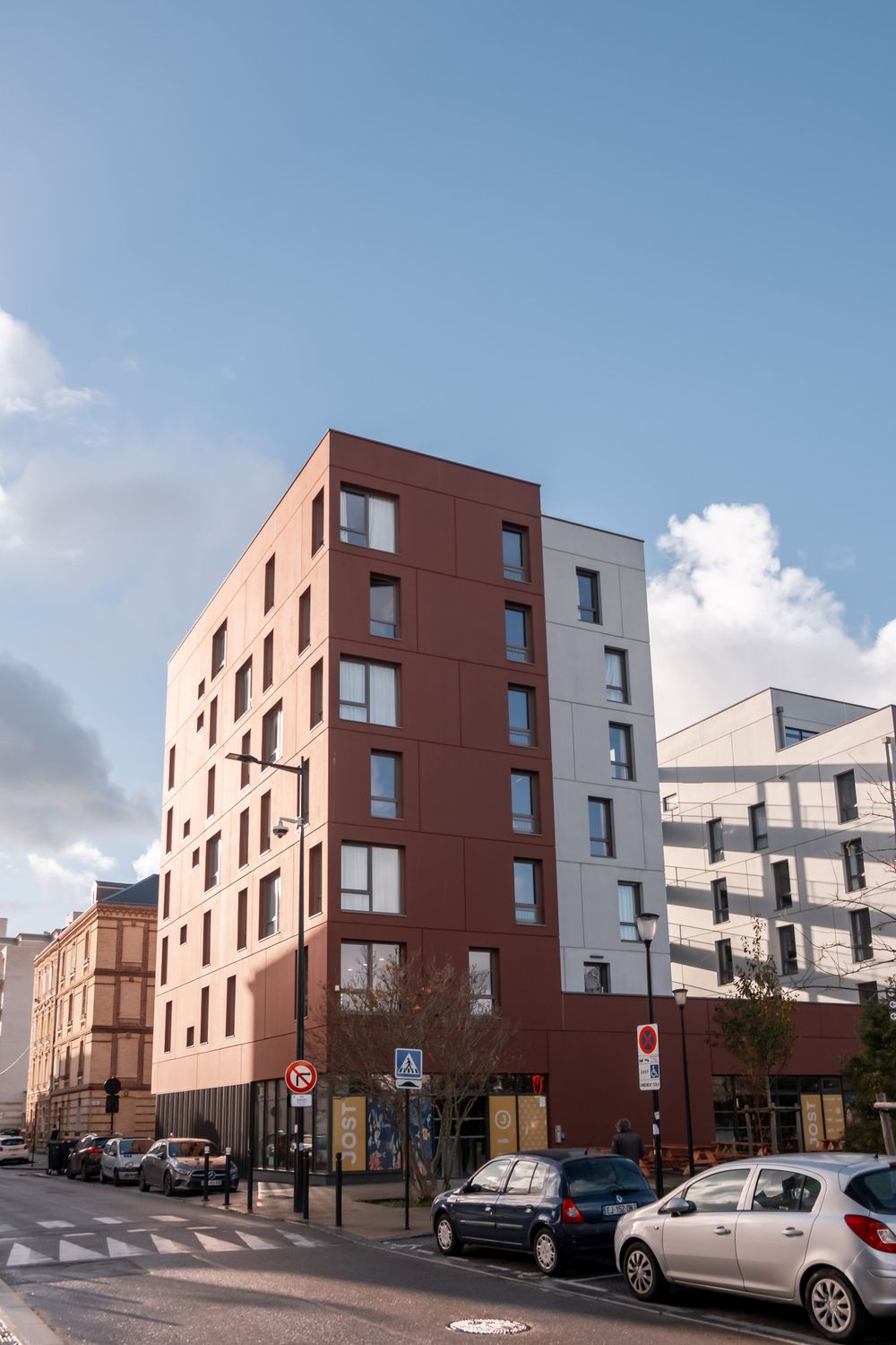 Contemporary red and white apartment building rising against blue sky in urban setting.