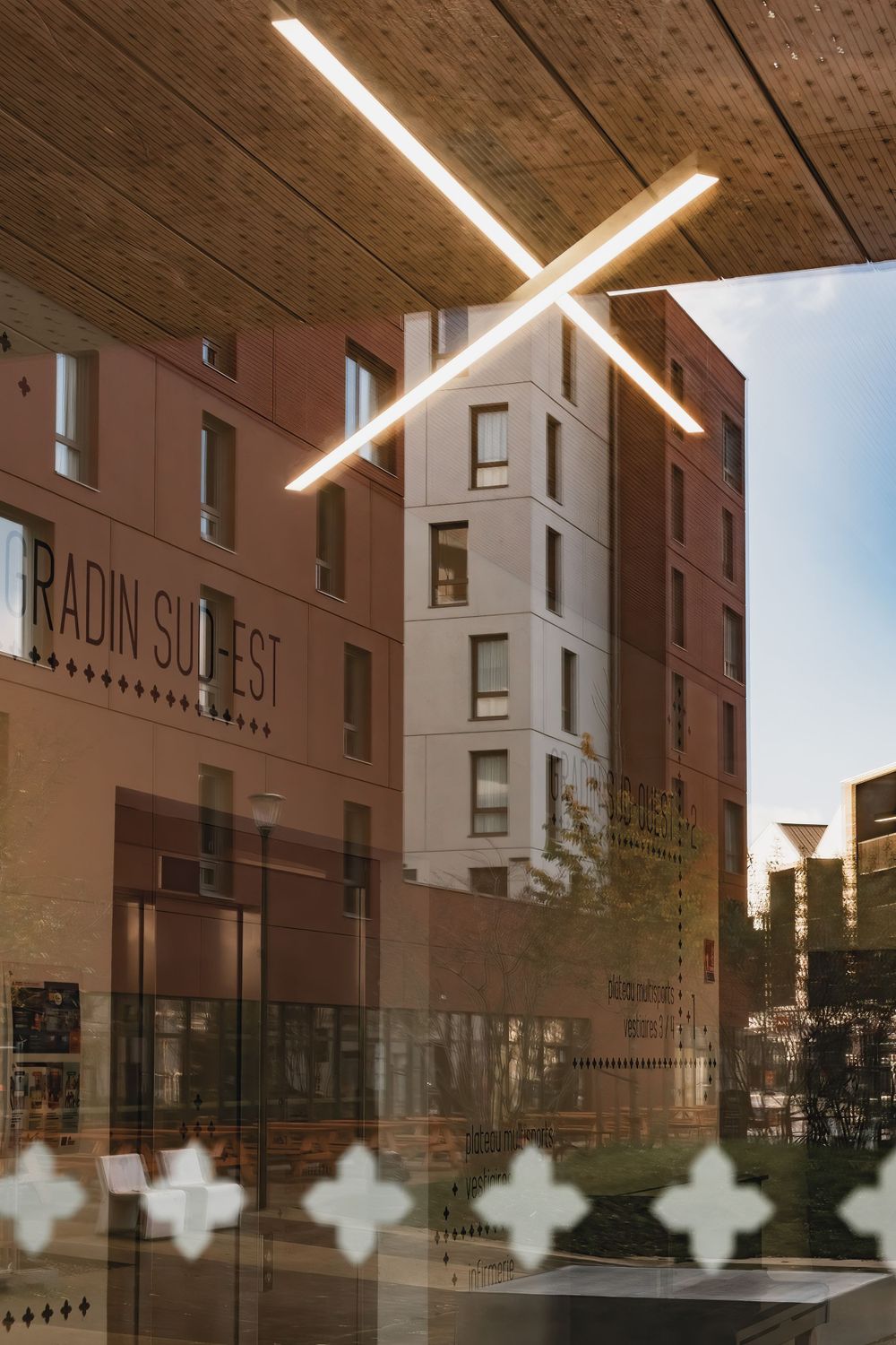 Modern building facade with illuminated cross-shaped light fixture and architectural details.