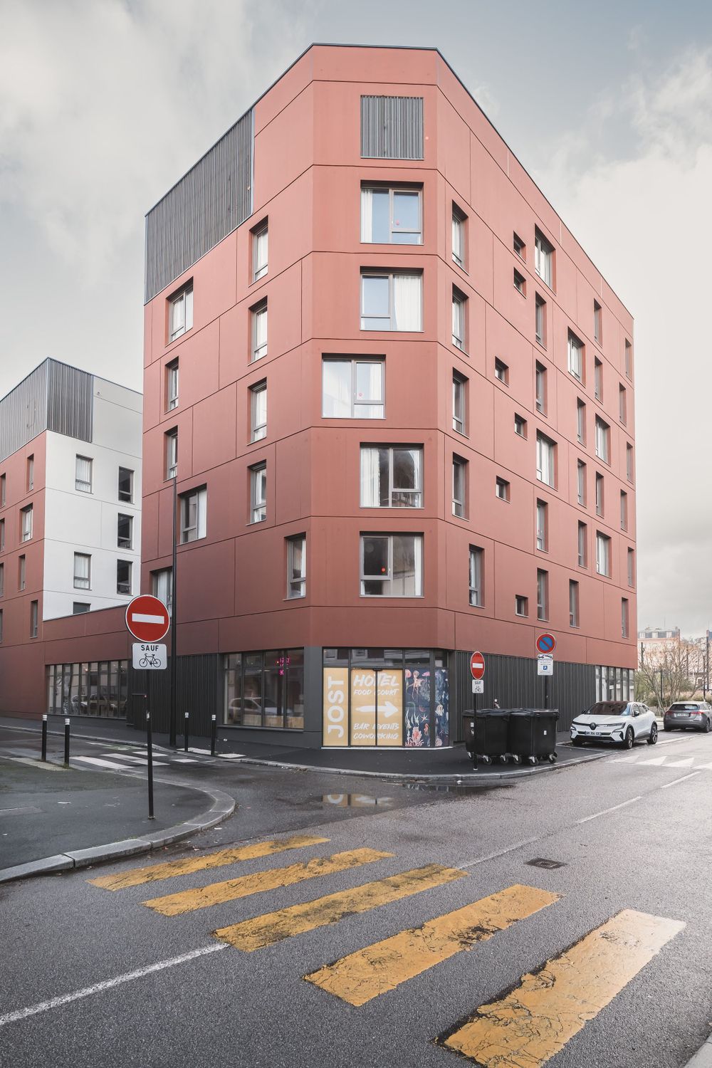 Modern salmon-colored apartment building with grey accents on a city street corner.