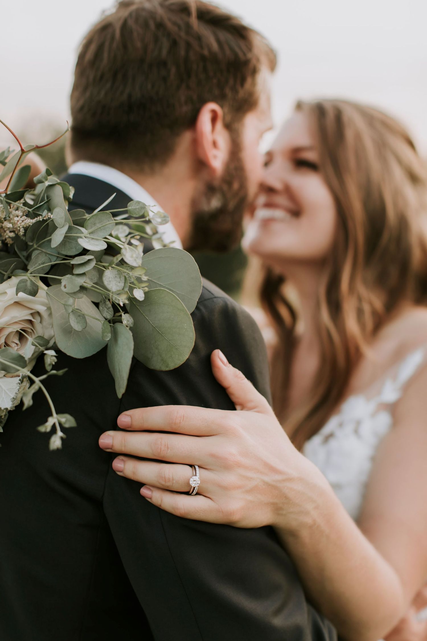 Bride and groom touching noses while displaying wedding ring on the groom's shoulder