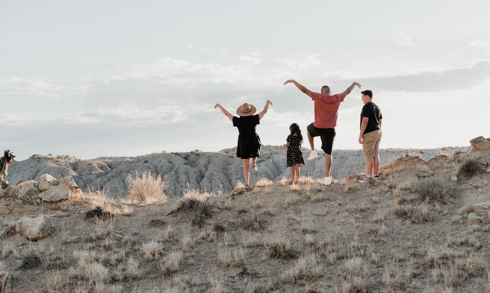 People celebrating with arms raised on hilltop against cloudy sky.