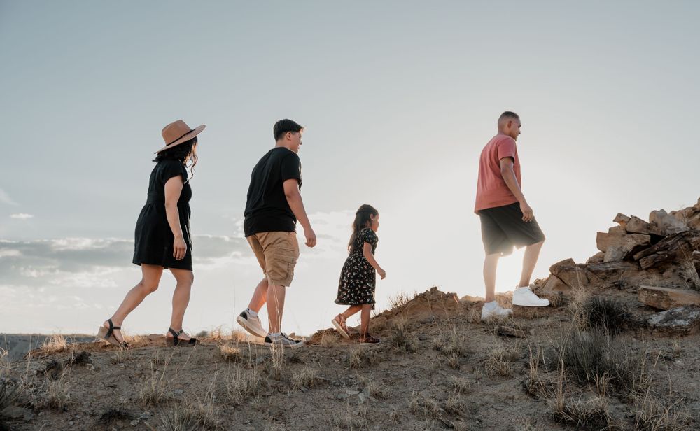 Group hiking along rocky ridge during sunset with ocean visible in background.