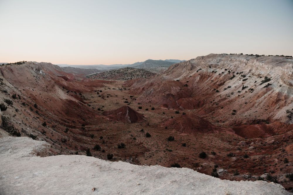 A dramatic red rock canyon landscape with snow patches under bright blue sky.