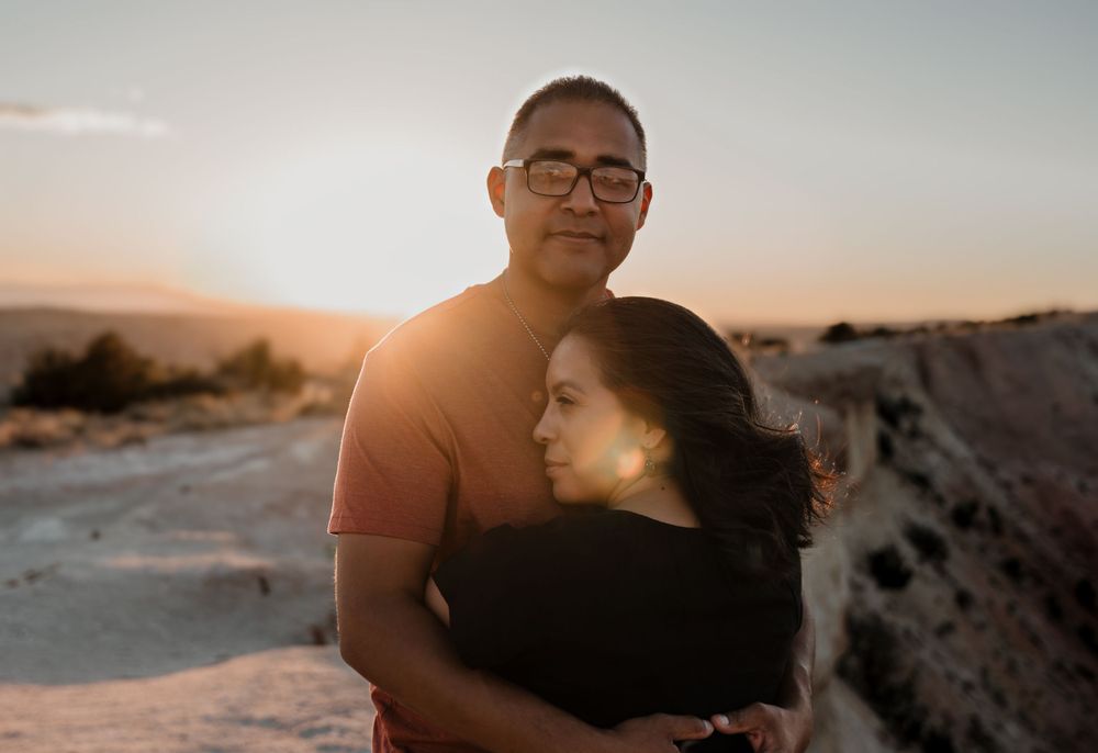 Two people embracing during sunset with desert backdrop and warm lighting.