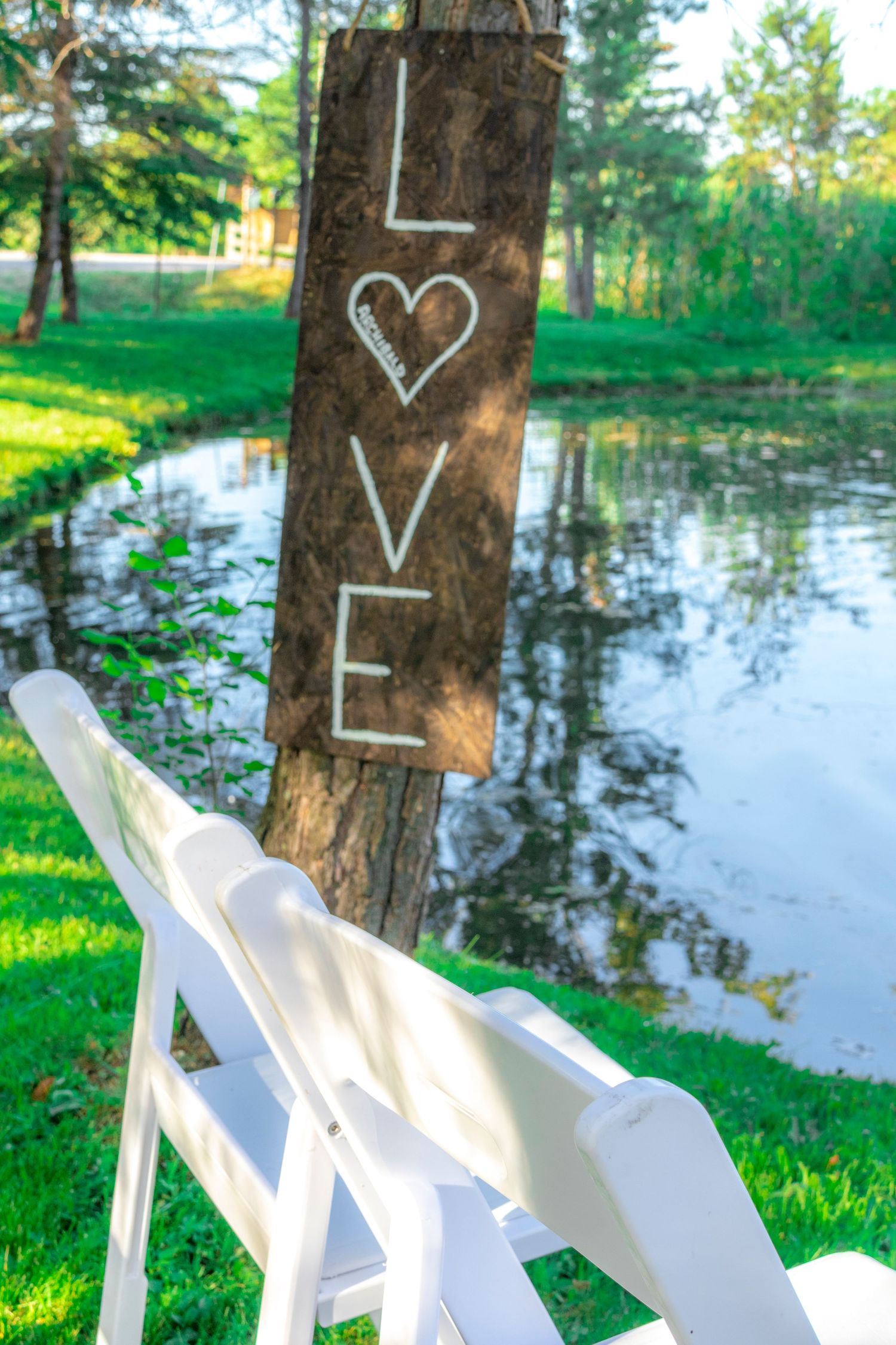 Wood love sign posted to a tree in front of a pond that reads Love