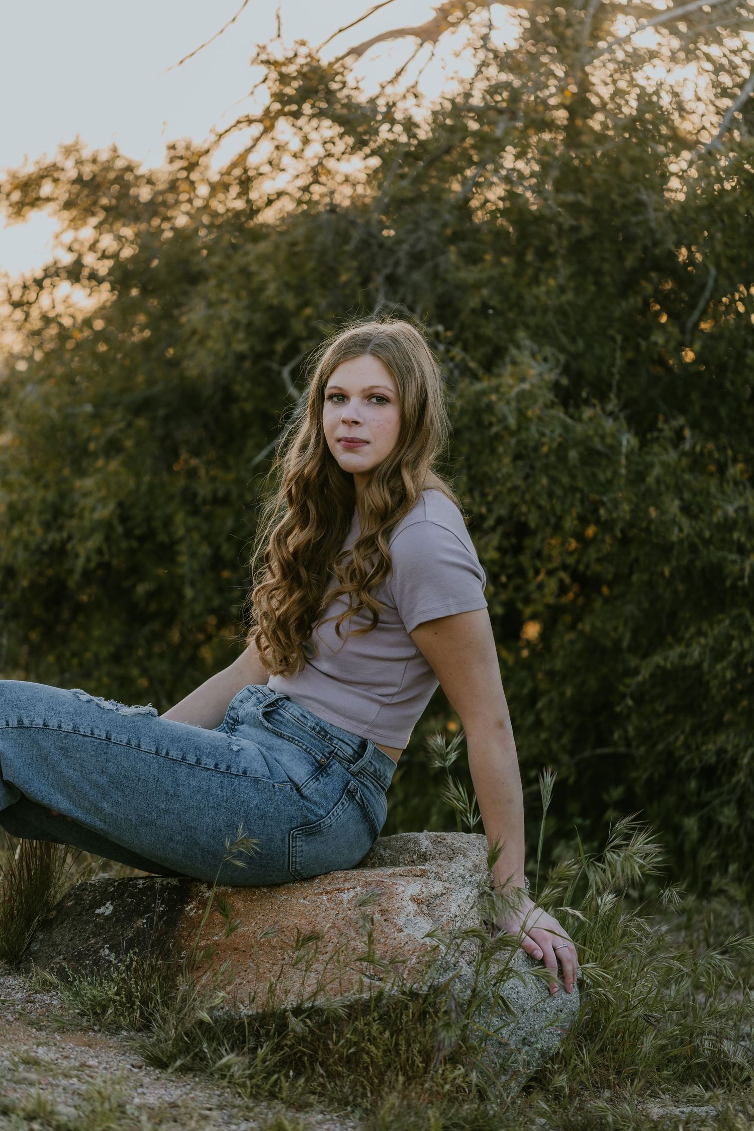 Person reclining on rocky terrain wearing blue jeans and light top at sunset.
