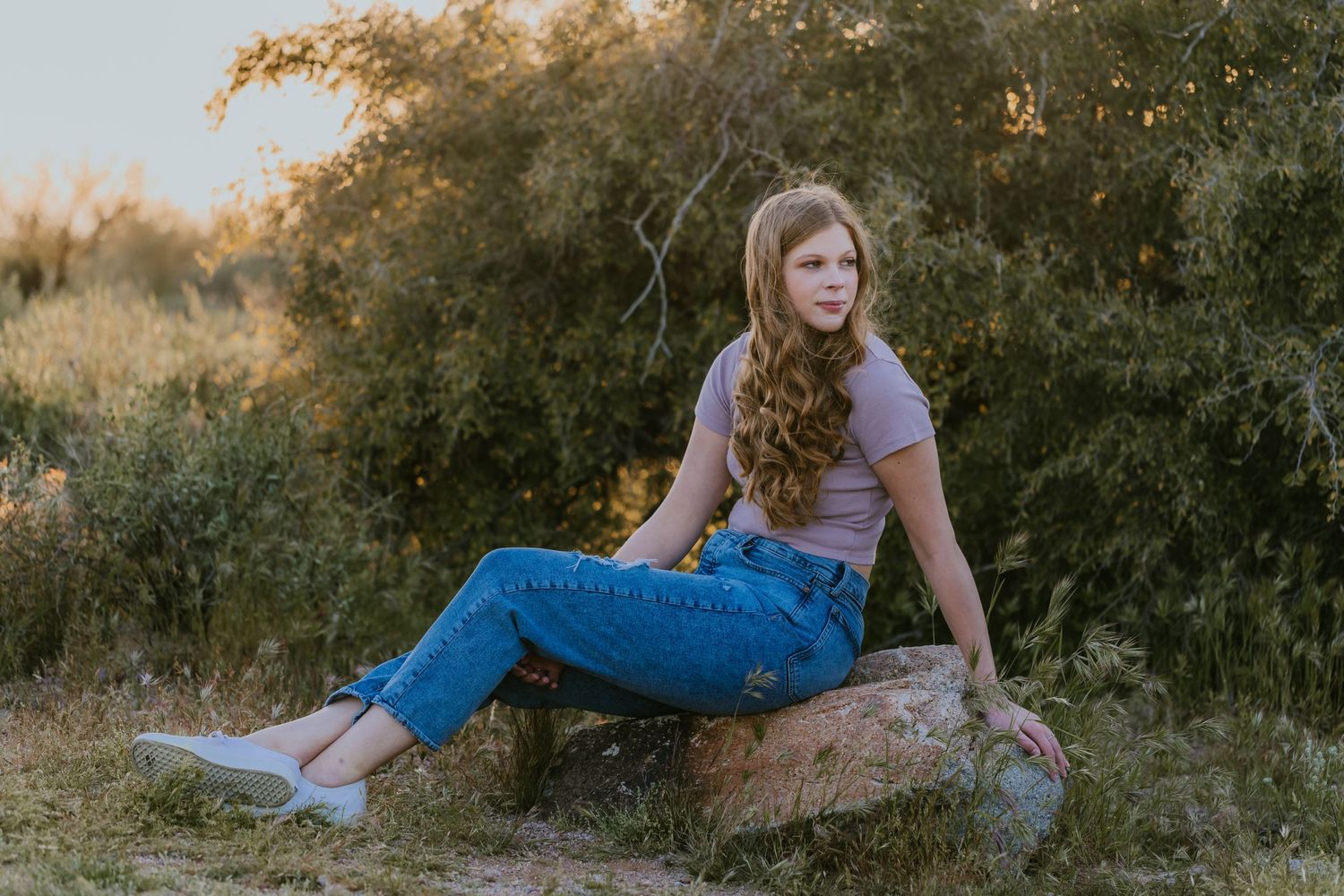Person in jeans and t-shirt posing against natural backdrop at sunset.