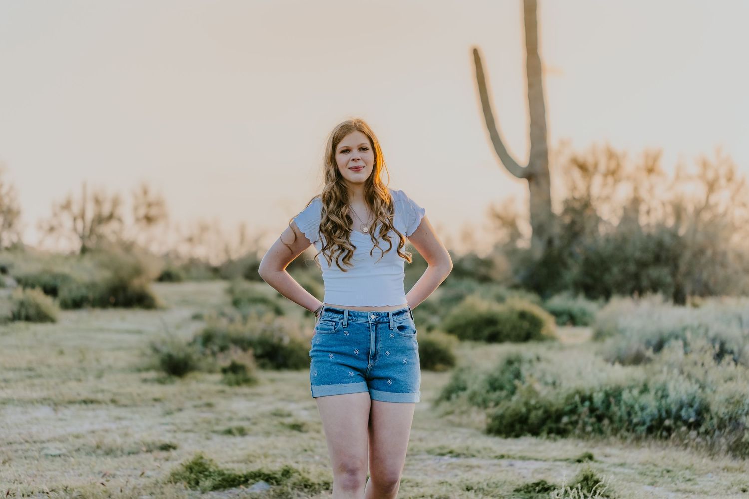 Person in denim shorts standing amid desert vegetation during golden hour photoshoot.