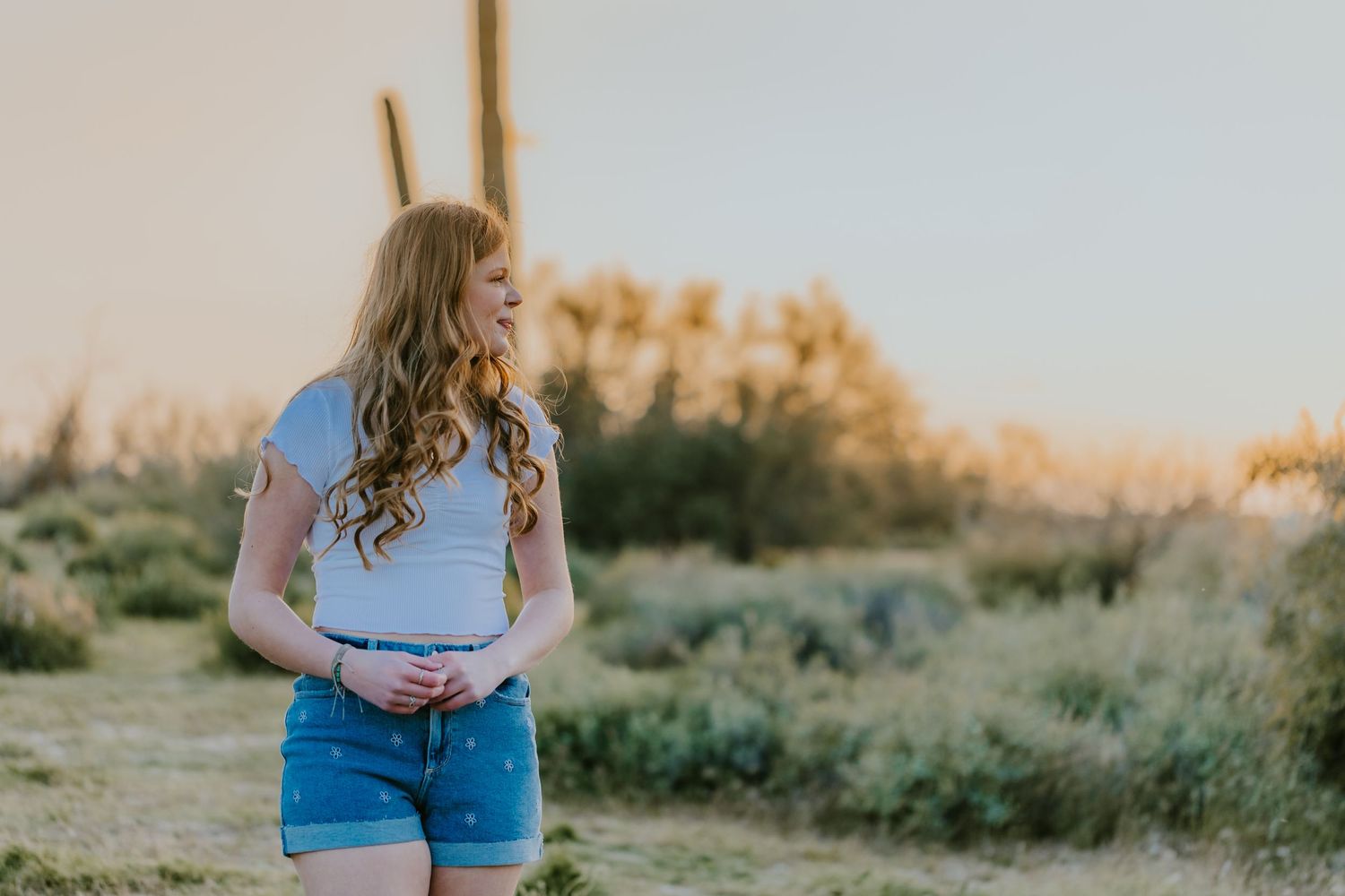 A casual portrait against a desert landscape with mountains and saguaro cacti at sunset.