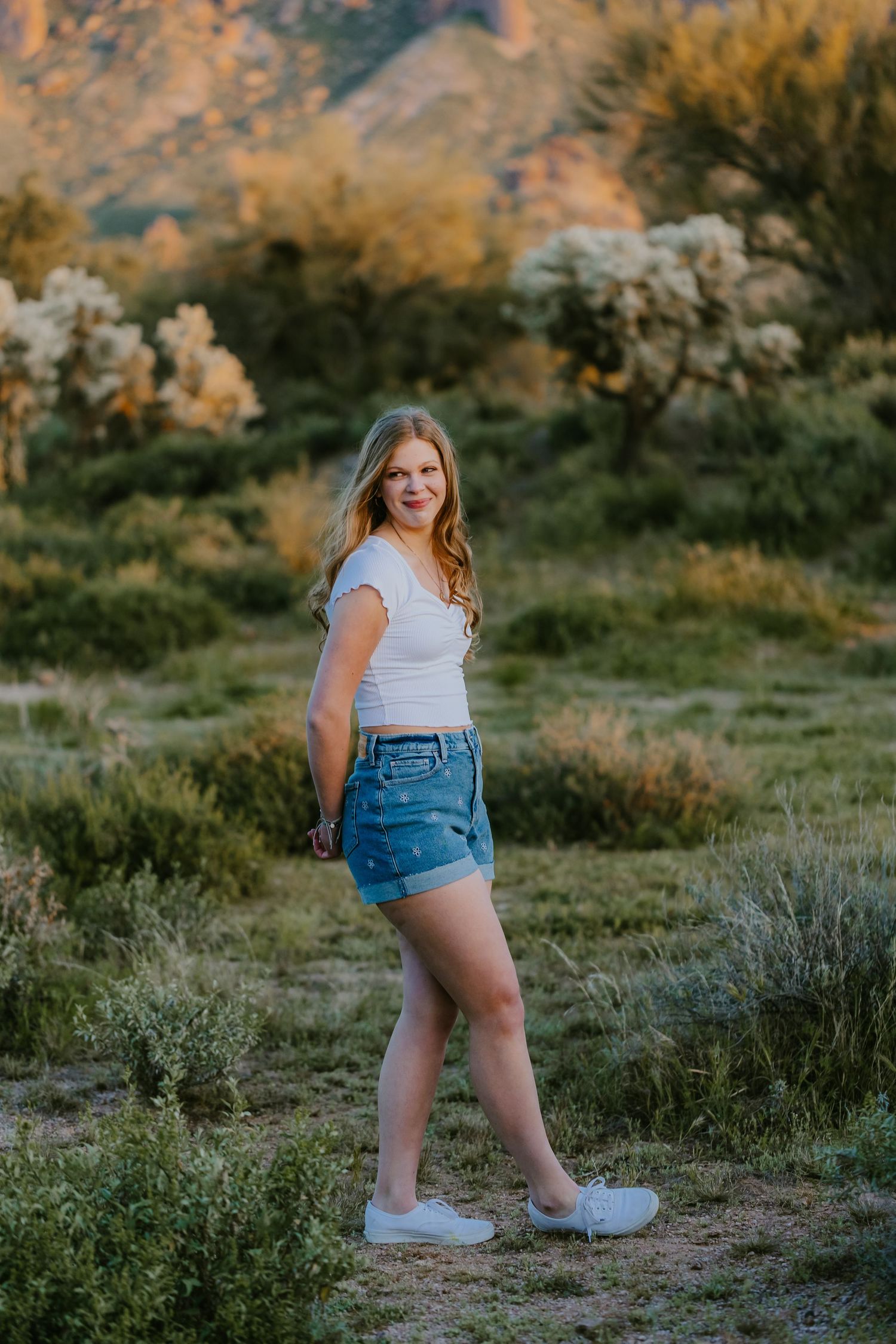 A casual summer outfit featuring denim shorts and white top against a desert landscape at golden hour.