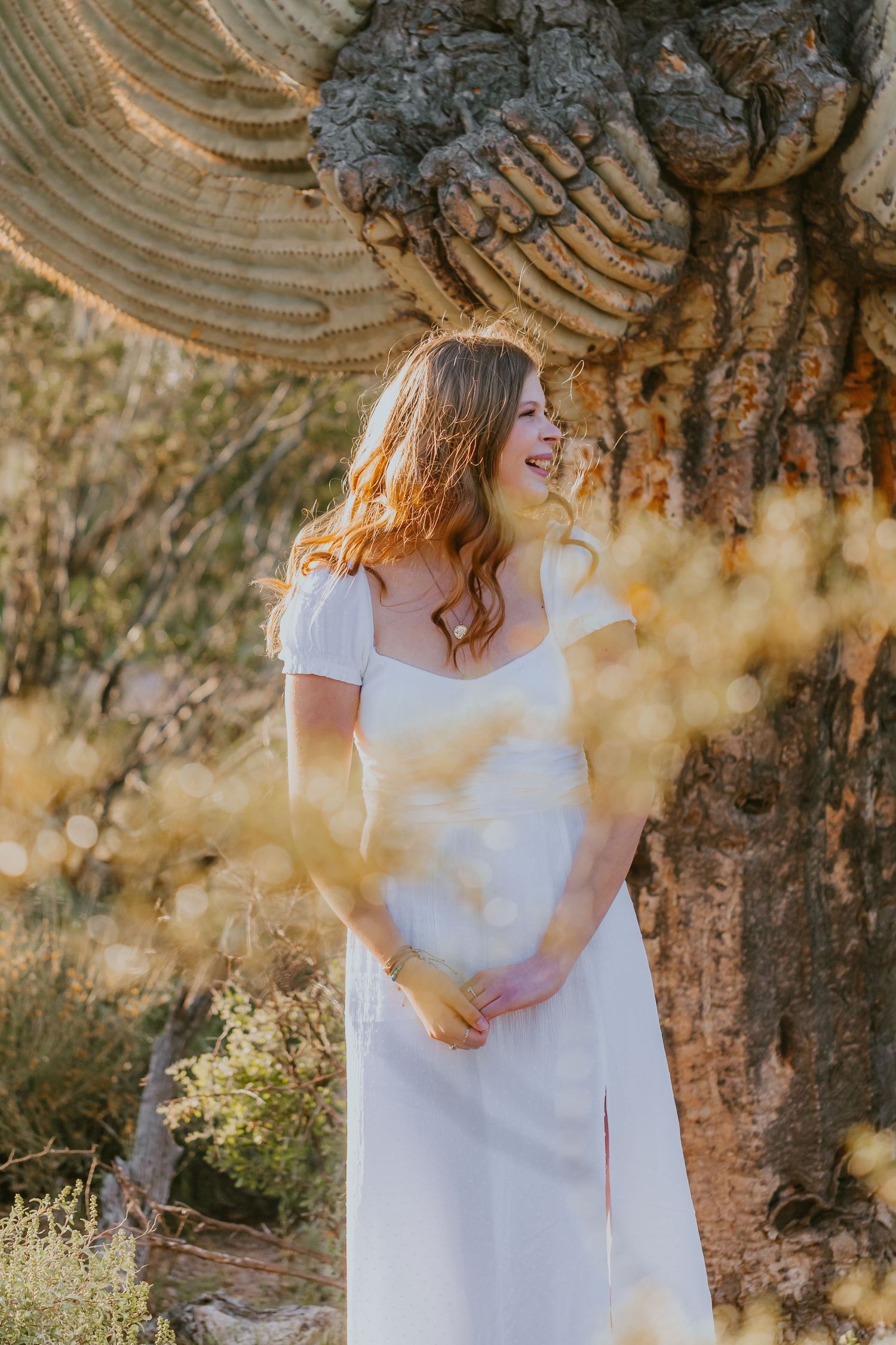 Elegant white dress portrait against textured rock formations in golden desert light.