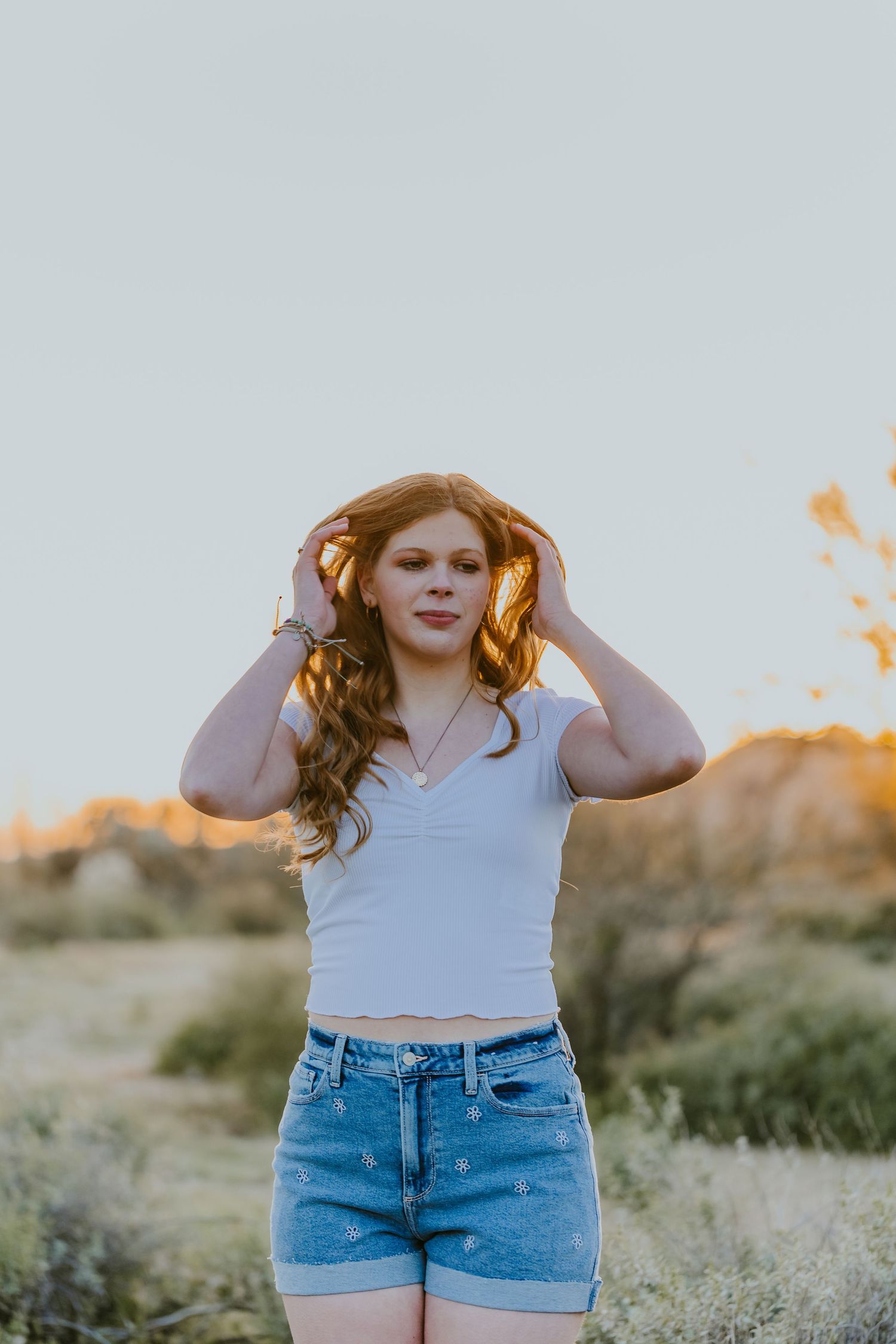 Candid outdoor portrait in white top and denim shorts during sunset in desert setting.